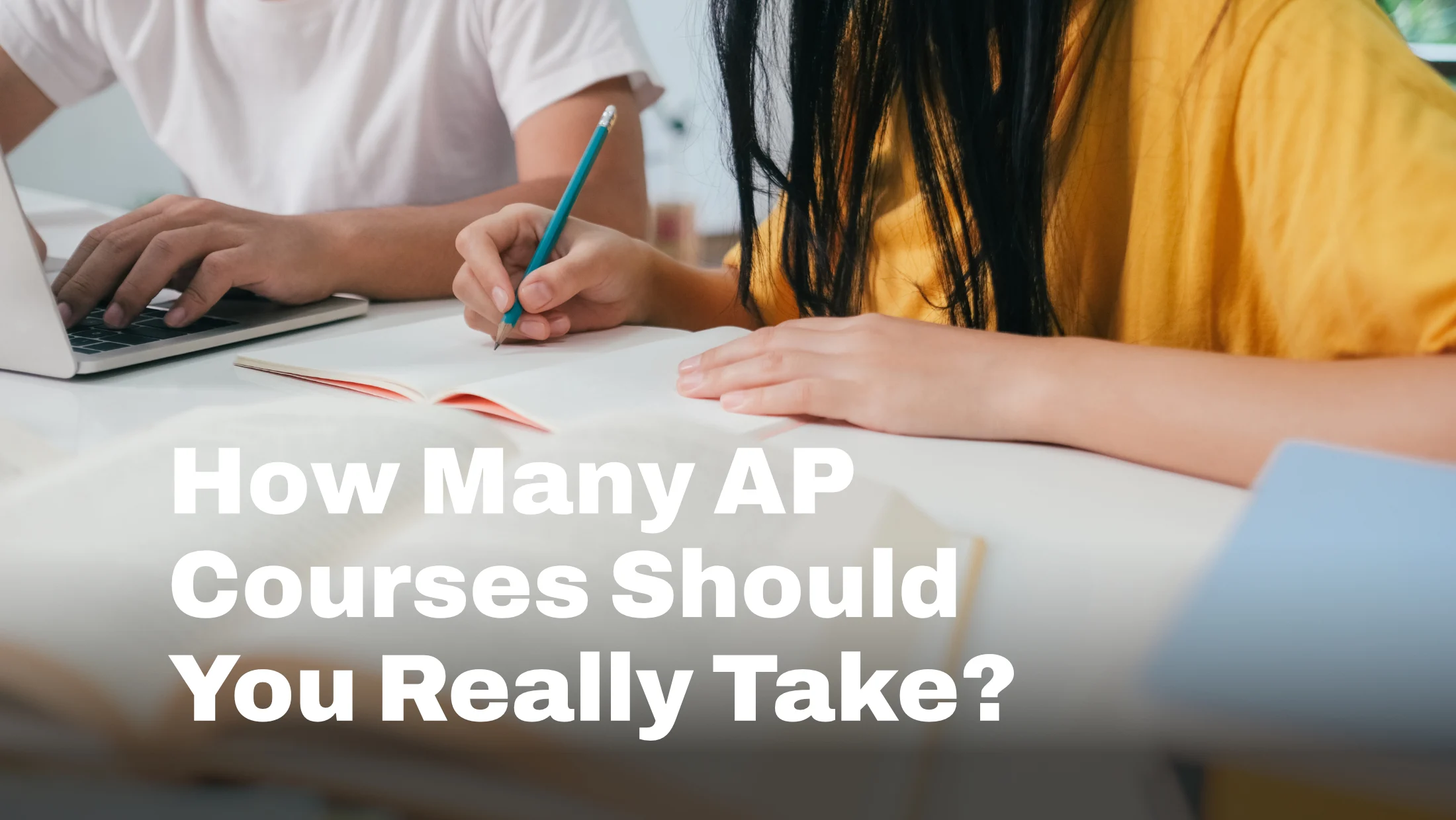 Two students' hands at a desk, one typing on a laptop and one writing in a notebook, with the words "How Many AP Classes Should You Really Take?'